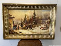Front view of the gilt framed Cornelius Krieghoff "Bilking The Toll" winter scene print set in a decorative carved gilt frame with light wear.