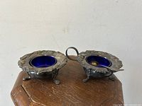 Pair of silver plated gothic three-legged salter pots with cobalt blue glass liners, one with handle visible, on wood surface