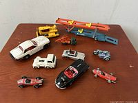 Group of 10 vintage diecast toy vehicles including cars, a motorcycle, tractor, bulldozer and a car transporter trailer in blue with orange ramps.