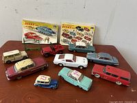 Wide shot showing all 10 vintage Dinky toy cars and 2 catalogues on wood surface.