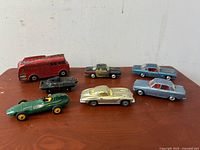 Top view photo of all seven vintage Dinky Toys diecast cars displayed on wood surface showing various colors and types including fire engine and racing cars.