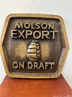 Front view of large vintage wooden Molson Export On Draft sign with raised lettering and ship emblem on hexagonal pressed wood panel, showing wood grain and patina.