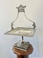 Photo of full Victorian silver plated brides basket card tray with handle and pedestal podium base, showing ornate floral design and overall shape.