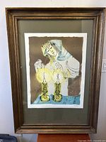 Framed lithograph artwork by Sami Briss showing a figure lighting two candles, photographed straight on with clear view of print, mat, and frame.