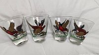 Front view of four clear Hazel Atlas Swanky Swig juice glasses with pheasant decoration in various poses.
