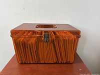 Closed amber plastic box with handle, showing front and latch closure