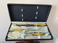 Vintage three-piece carving set inside open fitted case, showing knife, fork, and sharpening steel with faux horn-style handles on light blue satin lining.