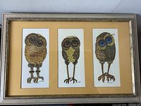 Front view of the framed triptych showing three stylized owl illustrations by Glenn Heath on mustard matting within a gray distressed frame.
