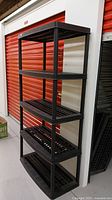 Full view of the black plastic shelving unit showing five shelves and vertical supports beside orange storage lockers.