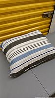 Striped pillow sham with blue, gray, white, and black nautical stripes, laying folded on a table.