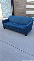 Front and side view of teal-blue 3-seater sofa placed outdoors, showing tight back, seat cushions, curved arms, and espresso legs.
