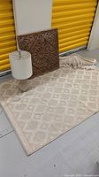 Wide photo showing all four items: lamp, carved wood artwork, folded cotton wall hanging, and wool area rug with geometric pattern