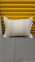 Standard pillow sham laying flat with embroidered vertical soft brown stripes on off-white linen-look fabric.