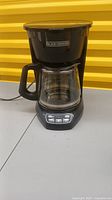 Front view of Black + Decker coffee maker showing overall design with glass carafe and control panel buttons.