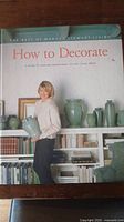 Front cover of 'How to Decorate' showing a woman holding pottery, shelves with books and vases in the background