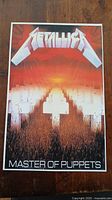 Front view of Metallica Master of Puppets poster showing white crosses and sunset background.