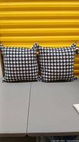 Two navy blue and off white houndstooth pattern toss cushions shown side by side against a yellow background.