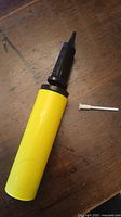 Full view of yellow cylindrical hand pump with black nozzle and white needle on wooden background