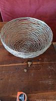 View of the large spun metal bowl showing the spiral woven design and size in proportional comparison to the measuring tape on the table.