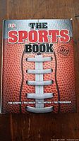 Cover of 'The Sports Book' 3rd Edition by DK, showing title and football textured design.