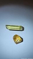 Two citrine crystals on white background, an elongated lemon yellow crystal and a smaller golden yellow rough crystal.