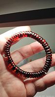Close-up photo of the bracelet held in hand, showing translucent deep maple amber beads with a glossy finish and uniform rounded shapes.