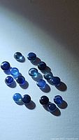 Top down photo showing 18 small round cabochon blue sapphires in natural lighting with some reflections.