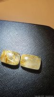 Photo shows two cushion cabochon cut golden rutilated quartz gemstones with visible golden needle inclusions.