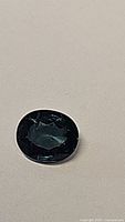 Close-up image of natural blue teal sapphire gemstone showing its oval cut and clarity against a plain background.