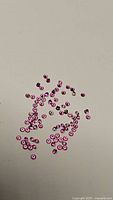 Photo showing multiple small round cotton candy pink sapphires scattered on a flat surface, highlighting their small size and color.