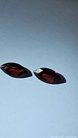 Photo of two marquis cut deep red garnet gemstones placed on a light background highlighting their color and cut.