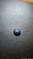 Top-down photo of a natural oval blue star sapphire showing a clear six-ray star effect on a dark textured background.
