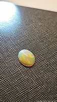 Photo of a polished oval cabochon Ethiopian opal with visible rainbow flash on a textured black background