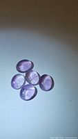 Six natural light purple oval cabochon amethyst gemstones displayed on a white background.