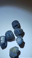 Photo showing six natural blue sapphire rough crystals with deep blue color and some inclusions.