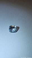 Single natural sky blue topaz gemstone, cushion cut, 6x6mm, under lighting showing facets and color.