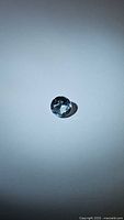 Photo of a round cut natural sky blue topaz gemstone on a white background, showing facet detail and color.