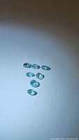 Seven oval cut lagoon blue Cambodian zircon gemstones arranged closely on white background showing their size and cut.