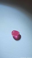 Close-up photo of pinkish-red natural ruby gemstone with faceted briolette cut, showing stone surface and color