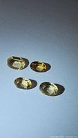Four oval cut golden citrine gemstones arranged on white background showing clarity and color differences