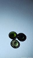 Three green tourmaline gemstones laid together on white background showing variations in green color and facet reflections.