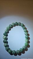 Natural spotted green jasper bead bracelet laid flat in circular shape showing full string of beads.