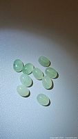 10 natural mint green oval cabochon cut kyanite gemstones shown on a light surface with lighting to reveal translucency and color.