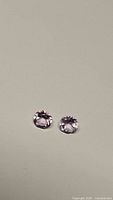 Photo showing two round-cut natural light pink amethyst gemstones placed next to each other on a plain background to highlight color and cut.