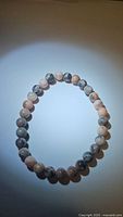 Photo of a natural pink zebra jasper bracelet featuring 6mm round beads with gray and black zebra-like striping on a pink base, stretchy design.