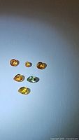 Six loose sapphires in various colors including orange, yellow, and green on a white background, showing size and color variation.