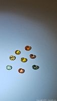 Seven small round faceted multicolored sapphires shown with bright lighting on white background
