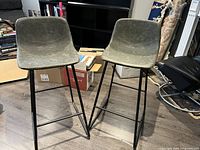 Front view showing two green leather barstools with black metal legs and footrests.