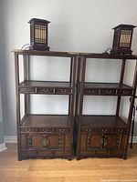 Front view of two antique Korean elm display shelves showing their overall structure with open shelving, drawers, and cabinet doors topped by small square lanterns.