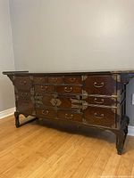 Front angle of antique Korean elm wood buffet showing multiple drawers, brass handles, and decorative brass corner accents.